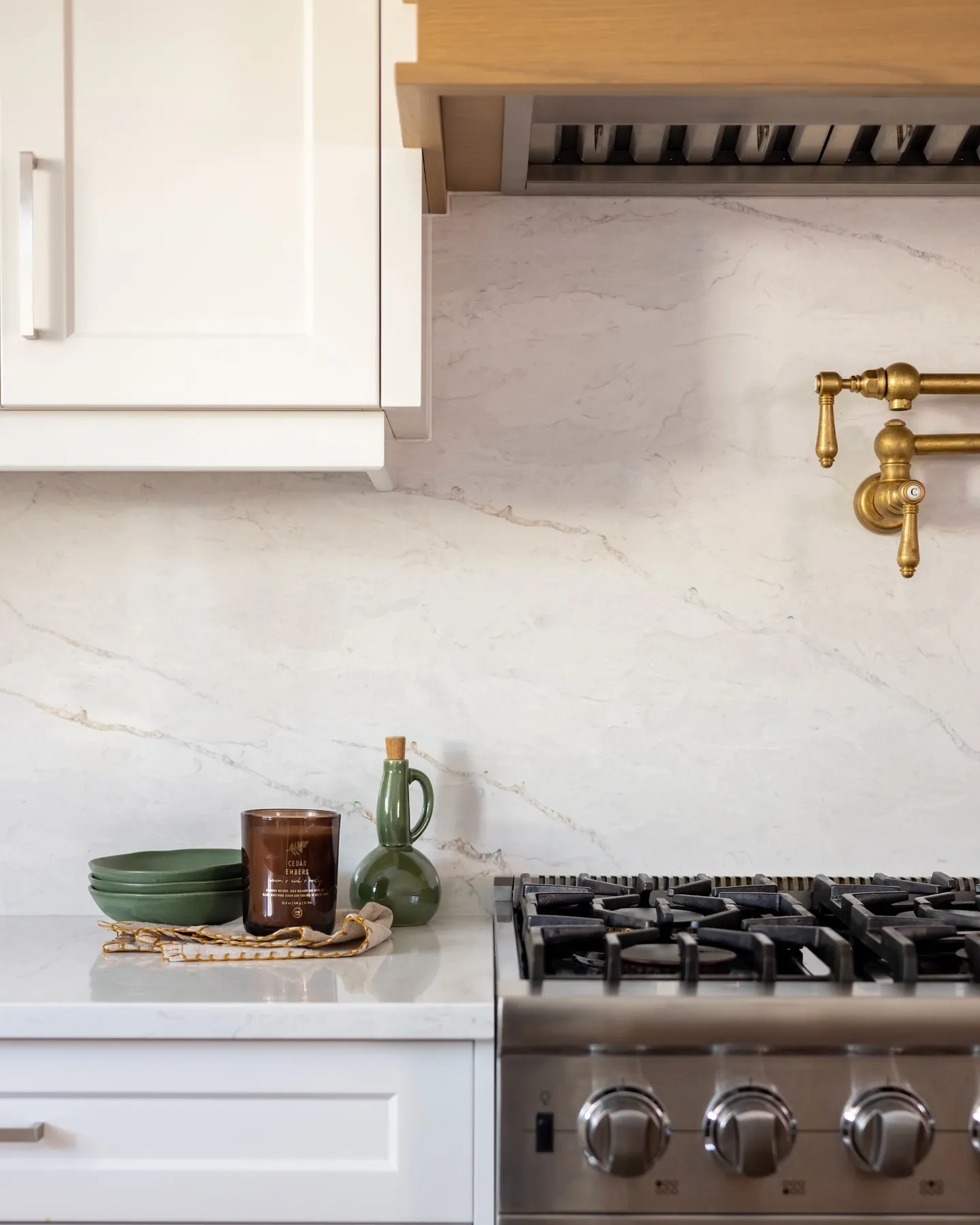 Marble backsplash and brass pot filler above a gas range, styled with ceramics