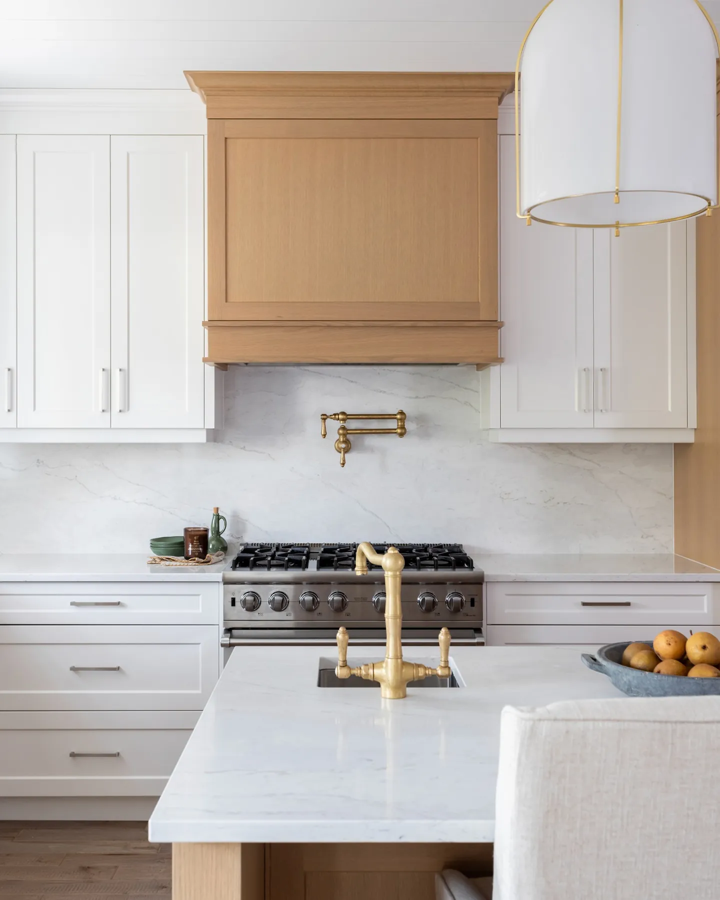 Range wall with a custom oak hood, brass pot filler and white shaker cabinetry