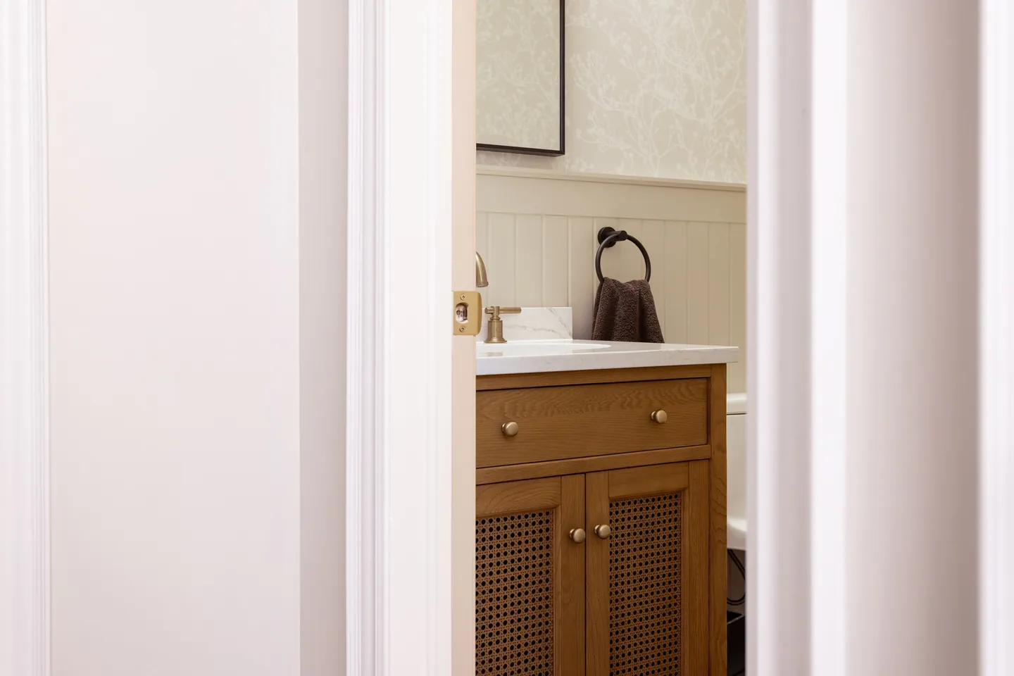 Powder room with a white oak cane-front vanity and patterned wallpaper