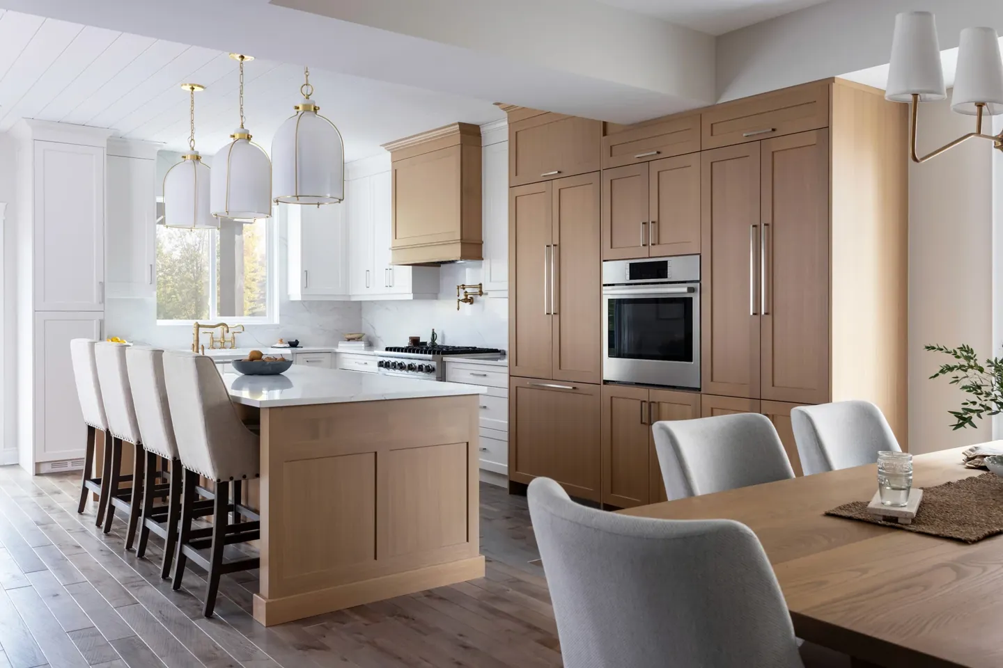 White oak kitchen with a quartz-topped island, upholstered stools and brass pendants