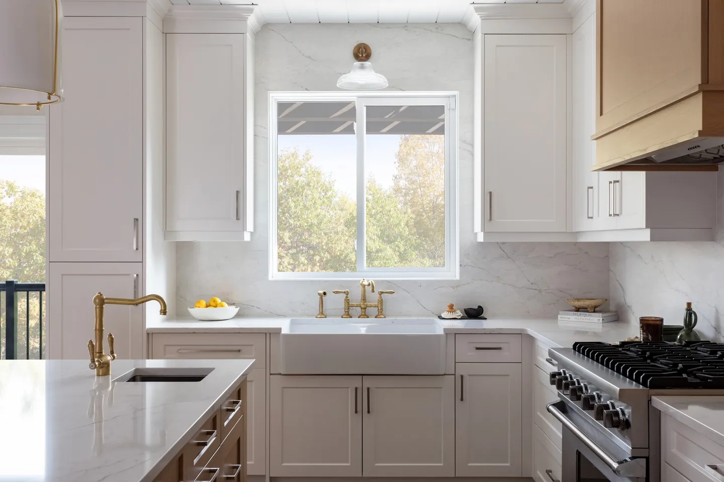White shaker kitchen with a farmhouse sink, brass bridge faucet and garden window